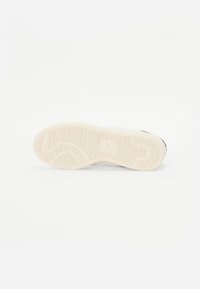 Hvid sneakersåls med tekstureret grebmønster, har en afrundet form og glatte kanter. Gummimateriale, lys cremede farve med mørke accenter.