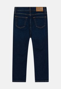 Jeans in denim blu scuro con una texture liscia, caratterizzati da un'etichetta in pelle marrone e due tasche posteriori con dettagli di cucitura discreti.