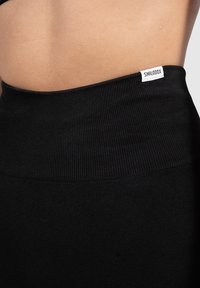 Zbliżenie talii osoby noszącej czarne prążkowane legginsy o wysokim stanie z małą białą metką marki "SMILODOX" na pasku.