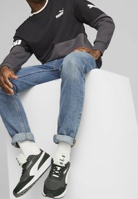 Czarna i szara koszula z długim rękawem z białymi akcentami, niebieskie dżinsy i czarne trampki. Na koszuli i butach znajduje się logo Puma.