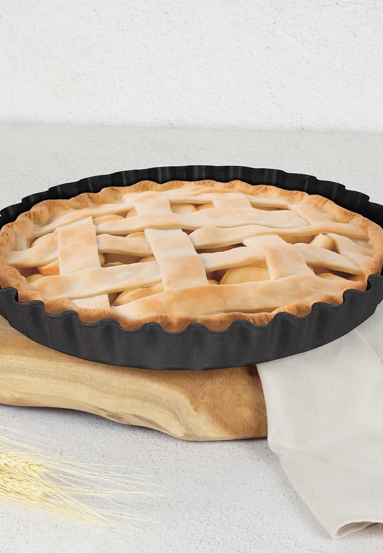 Tarte ronde avec une croûte en treillis dans un moule noir à bord cannelé, placée sur une planche en bois avec une serviette en tissu léger à côté.