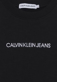 Černá mikina s kulatým výstřihem vyrobená z hladké látky, na hrudi zdobená bílým vyšitým logem "CALVIN KLEIN JEANS".