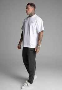 White cotton t-shirt with short sleeves, paired with dark gray pinstriped trousers. White sneakers with textured laces complete the outfit.