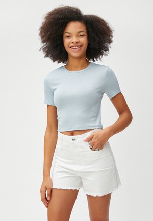 Hellblau gestreiftes Kurzarm-Crop-Top kombiniert mit weißen Denim-Shorts, die einen fransigen Saum und einen frontalen Knopfverschluss aufweisen.