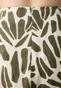 Una gonna beige con un motivo astratto verde, dotata di una zip sul retro e con una silhouette dritta, realizzata in tessuto leggero.