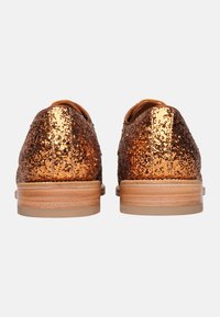 Scarpe con glitter bronzo scintillante, con rivestimento interno in tan morbido, punta arrotondata e tacco in legno chiaro. La vista posteriore mostra la texture superficiale luccicante.