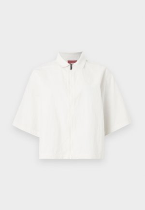 Veste blanche à manches courtes avec fermeture éclair à l'avant et petit col, présentée à plat sur un fond uni.