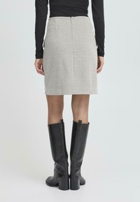 Grå herringbonekjol med slim fit, knälång, bakdragkedja, tillsammans med l�ånga svarta läderstövlar och en svart långärmad topp.