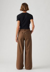 Schwarzes, kurzärmeliges Oberteil mit tailliertem Schnitt, kombiniert mit lockeren, hoch taillierten braunen Hosen mit zwei Gesäßtaschen. Minimalistischer Stil.
