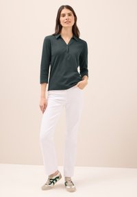 Tmavě zelená polokošile s dlouhým rukávem a límečkem, doplněná bílými rovnými kalhotami a šedozelenými teniskami.