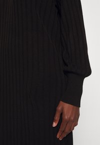 Abito nero a costine con maniche lunghe, vestibilità comoda e superficie testurizzata. Presenta un delicato motivo a strisce verticali.