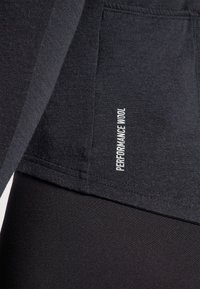 Čierne športové tričko s jemnou textúrou, s detailom švov a bielou etikettou "PERFORMANCE WOOL" na boku.