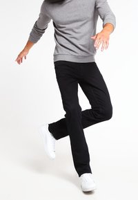 Czarne dżinsy o dopasowanym kroju, w połączeniu z jasnoszarym, długim rękawem, oraz białymi sneakersami. Dżinsy mają standardowe kieszenie i zamek błyskawiczny.