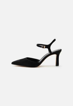 Zapato de tacón alto de ante negro con punta afilada y una fina correa en el tobillo con una pequeña hebilla dorada.