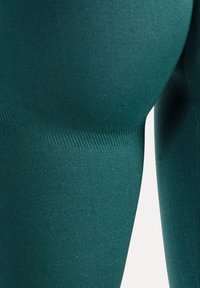 Close-up van petrolblauwe gebreide stof met gedetailleerde textuur en naadloze constructie.