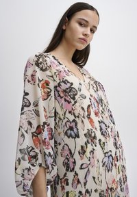 Schwingendes Blumenkleid aus leichtem Stoff mit V-Ausschnitt, Glockenärmeln und einer Mischung aus bunten Blumenmustern auf einem cremefarbenen Hintergrund.