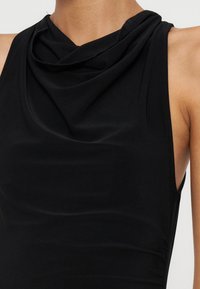Haut noir sans manches avec un col bénitier drapé porté par une personne aux épaules et au cou visibles.