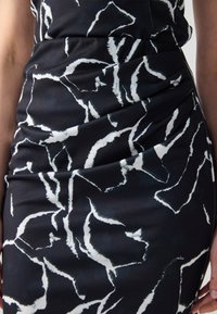 Abito nero con motivi astratti bianchi; presenta arricciature per texture e forma, realizzato in un tessuto liscio. La silhouette aderente mette in risalto la forma.