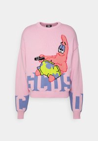 Pull rose en maille avec le personnage de dessin animé Patrick l'Étoile tenant une télécommande, et de grandes lettres bleues en blocs "GCDS" sur le devant et les manches.
