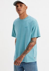Tricou din bumbac de culoare albastru deschis, cu guler rotund și mâneci scurte; prezintă un logo mic Levi's brodat în același ton pe piept.