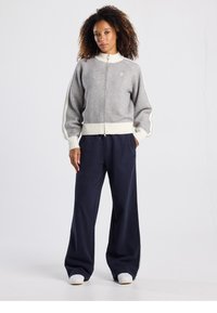 Pull gris à fermeture éclair avec accents crème et poignets côtelés, assorti à un pantalon large bleu marine et des baskets claires. Design simple, coupe décontractée.