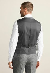 Gray fabric vest with a smooth texture, featuring a rear buckle for fit adjustment, worn over a white long-sleeve shirt, paired with gray trousers.