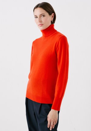 Roter Strickrollkragenpullover aus weichem Material, mit taillierter Silhouette und langen Ärmeln. Kombiniert mit navy-blauen gestreiften Hosen.