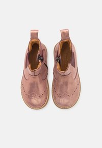 Różowe skórzane botki dziecięce za kostkę z ozdobnym detalem w stylu brogue, bocznymi zamkami błyskawicznymi i brązowym skórzanym wykończeniem. Okrągły nosek i gumowa podeszwa.