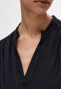Schwarze Bluse mit vertikalen Streifen, weicher Textur, Stehkragen und Knopfverschluss. Sie hat eine schmale Passform und einen subtilen Glanz.