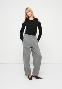 Top negro de manga larga con hombros descubiertos, combinado con pantalones anchos de color gris claro. La modelo lleva tacones negros de punta estrecha.