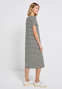 Striped dress in black and cream; short sleeves, relaxed fit, knee-length, with side slits. Worn with white sneakers. Smooth fabric texture.