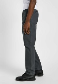 Szare bawełniane spodnie o prostym kroju, z delikatnymi detalami szycia, kieszeniami po bokach i zestawione z czarnymi sznurowanymi butami.