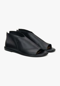 Czarne skórzane buty na otwartym palcu o gładkiej fakturze, zaokrąglonych krawędziach i niskiej podeszwie. Minimalistyczny design z wyciętymi bokami.