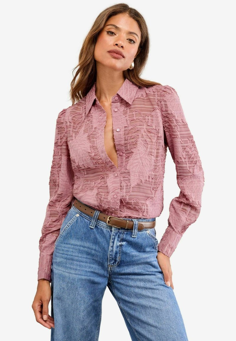 Rose-colored blouse with textured leaf patterns, button-down style, and long sleeves. Paired with high-waisted blue jeans and a brown belt.