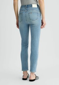 Jeans de mezclilla de color azul claro con un corte ajustado, cintura media, bolsillos traseros y dobladillos enrollados. Combinados con zapatos de eslora de patrón blanco y negro.