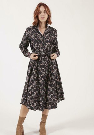 Robe chemise florale noire, avec des manches longues, des boutons à l'avant et une taille ceinturée. Présente une jupe fluide et de petits motifs floraux multicolores.