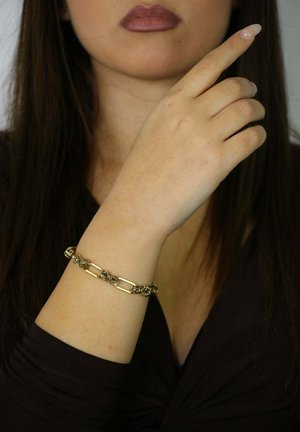 Pulsera de oro con elementos rectangulares entrelazados y ornamentados. Se lleva en la muñeca, con un diseño de textura suave y un brillo metálico.