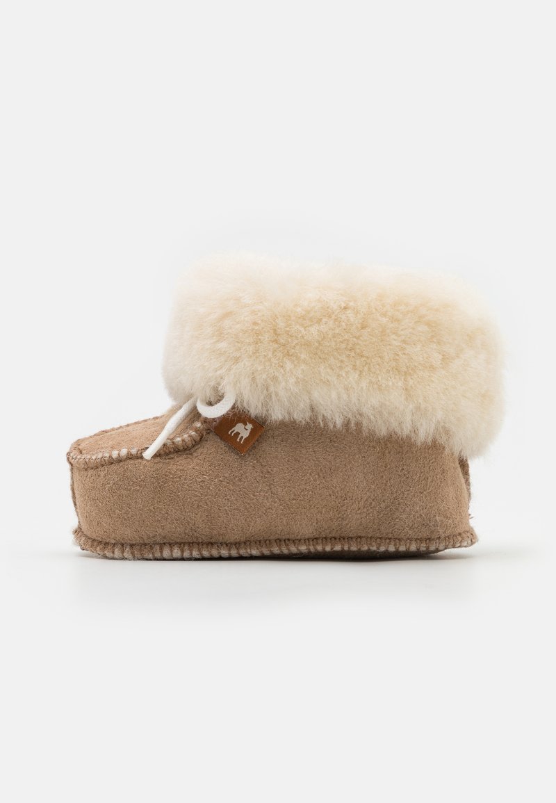 Tan suedep slipper med en fluffy kremfarget faux fur mansjett, rund tå, og hvite sømdetaljer, med et lite brunt merke på siden.
