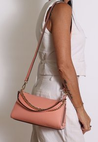 Borsa a tracolla in pelle rosa con finitura texturizzata, dettaglio in catena dorata e tracolla rimovibile. Forma rettangolare con angoli arrotondati.