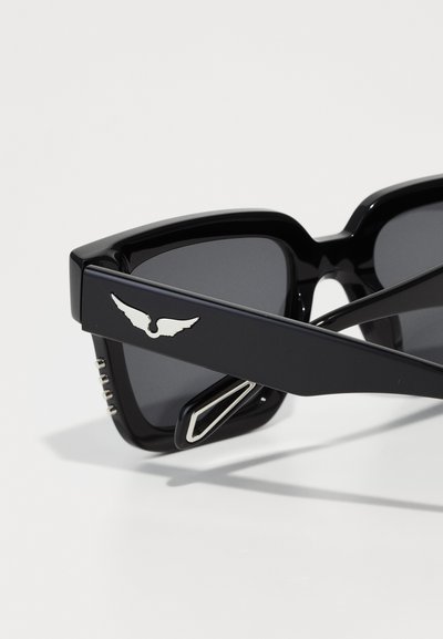 Occhiali da sole neri con montatura spessa, lenti scure e logo argentato a forma di ala sul lato. Accentuati da dettagli metallici sulle aste.