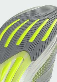 Semelle de chaussure affichant un motif texturé gris avec des accents jaunes vifs. Présente un design flexible et un profil de semelle varié pour une traction optimale.