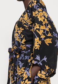 Florale kimono van zwarte stof met gele en paarse bloemenpatronen, wijde mouwen, een strikceintuur en een zachte textuur.
