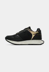 Baskets de sport noires et dorées avec une semelle blanche éclaboussée, un laçage sur le devant et le texte "Depuis 1981" au talon.