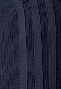 Närbild av mörkblått stickat tyg med växelvis breda och smala vertikala ribbor samt strukturerade ränder.