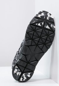 Sort atletiksål med en tekstureret, multidirektionel slidbane med hvide accenter og en let kurve for støtte.