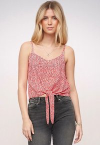 Rood met bloemenpatroon, mouwloos topje met een V-hals en strikdetail aan de voorkant, gemaakt van lichtgewicht stof; gecombineerd met donkergrijze jeans.