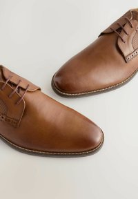 Chaussures en cuir marron avec une finition lisse, dotées de bouts ronds, de lacets et d'accents latéraux texturés. Semelle cousue avec une légère brillance.