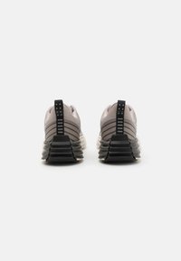 Um par de ténis com parte superior em malha cinza e sola de borracha preta, com riscas horizontais no calcanhar e uma alça para fácil calçar.