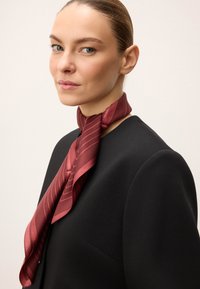 Eșarfă de mătase în bordou cu nuanțe profunde, având dungi diagonale. Textura moale se așază elegant în jurul gâtului, fiind asortată cu un top negru ajustat.