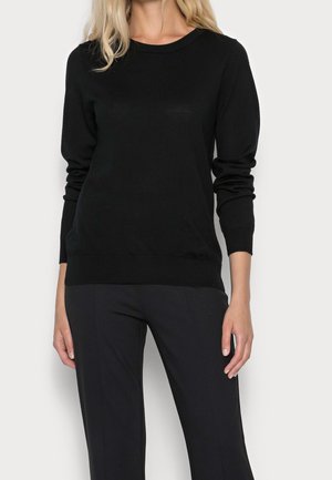 Black sweater made of a soft material, featuring a round neckline and long sleeves, with a fitted waist and ribbed cuffs. Paired with black trousers.